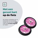 Twee roze zijwieltjes met zwarte banden voor kinderfietsen.