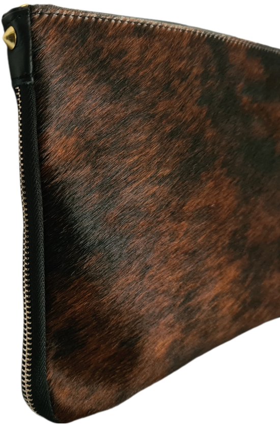 Close-up van een bruine en zwarte koeienhuid clutch met gouden detail aan de zijkant.