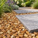 Grijze betonnen tegels, omzoomd door bruin-beige rivierkiezels met houtnerf-achtige patronen en groene planten.