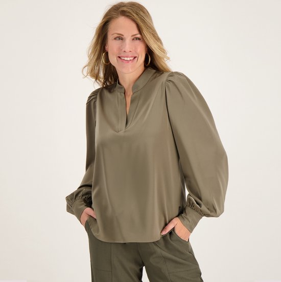 Model in een olijfgroene top met pofmouwen en bijpassende broek, handen in de zakken.