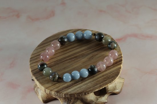 Armband van afwisselende blauwe, roze en donkere edelsteenkralen op een houten voetstuk.