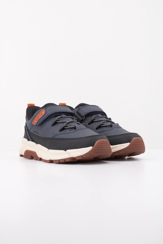 Donkerblauwe lage sneakers met oranje accenten, klittenbandsluiting en veters. Zwarte en crèmekleurige zool met bruine buitenzool.