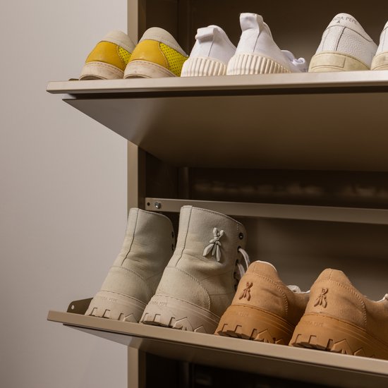Een schoenenkast met twee planken. Bovenop staan gele en witte sneakers. Op de onderste plank staan beige enkellaarzen en bruine lage schoenen met logo.
