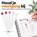 Vier teststrips met kleurverloop van donkerroze tot lichtroze, naast een open notitieboekje met ketose-metingen.