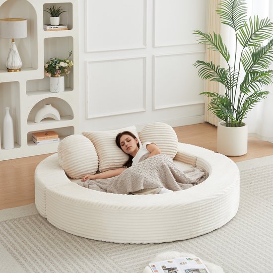 Vrouw slaapt op rond beige ribfluwelen dagbed met deken en kussens.