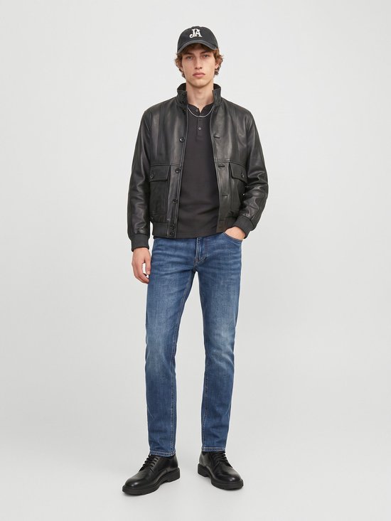 Model draagt een zwarte leren jas, donkergrijze top, blauwe jeans en een pet met 'JA' opdruk.