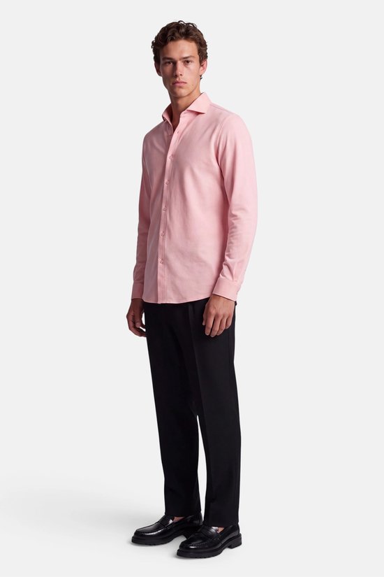 Model draagt een roze piqué overhemd met zwarte broek en zwarte loafers, volledig zicht.
