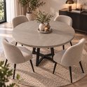 Ronde eettafel met een grijs houten blad en zwart metalen kruisvoet. Omringd door vier beige bouclé eetkamerstoelen.