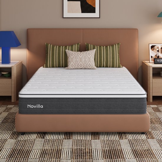 Novilla matras in een slaapkamer op een bed met bruin hoofdbord, omringd door kussens en nachtkastjes.