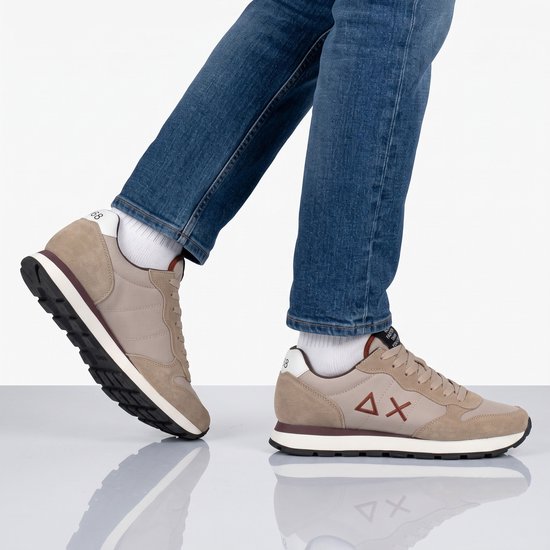 Beige sneakers gedragen onder een blauwe jeans, met focus op het Delta-X logo aan de zijkant.