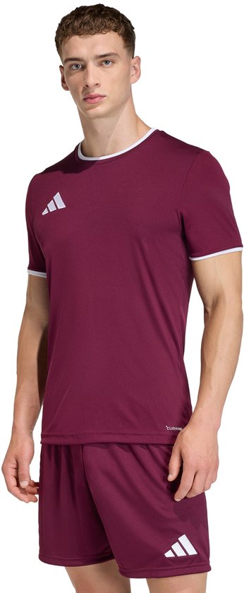 Man met bordeauxrood sportshirt en korte broek, beide met witte Adidas logo's. Hij draagt witte biesjes.