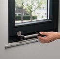 Hand bedient een zwart-metalen raamuitzetter gemonteerd op een donker raamkozijn.