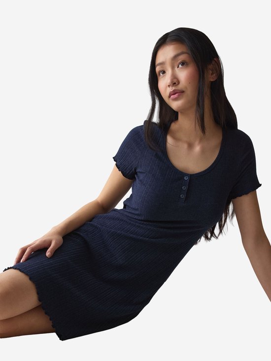 Zittend model in een donkerblauwe, geribbelde nachtjapon met knoopsluiting en korte mouwen met ruches.