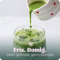 Groene matchathee wordt uit een kannetje met hartjes in een glas met ijsblokjes gegoten. Tekst: Fris. Romig.