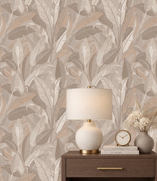 Behang met beige en taupe bladmotief achter een nachtkastje met een lamp, klok en boek getiteld The Kinfolk Home.