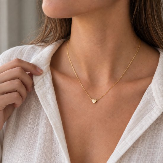 Gouden ketting met een klein, glanzend hartvormig hangertje op een dunne gouden schakelketting.