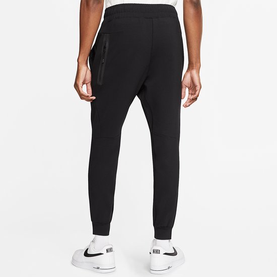 Zwarte Nike Tech Fleece joggingbroek met ritssluiting op de zak op het rechterbeen, gedragen door een man.
