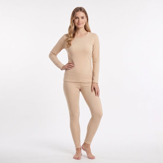 Een blonde vrouw staat in een beige thermopak met lange mouwen en legging.
