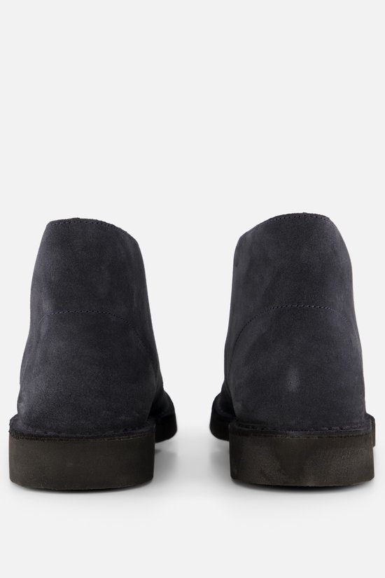 Achterkant van twee donkerblauwe suède desert boots met zwarte zolen.