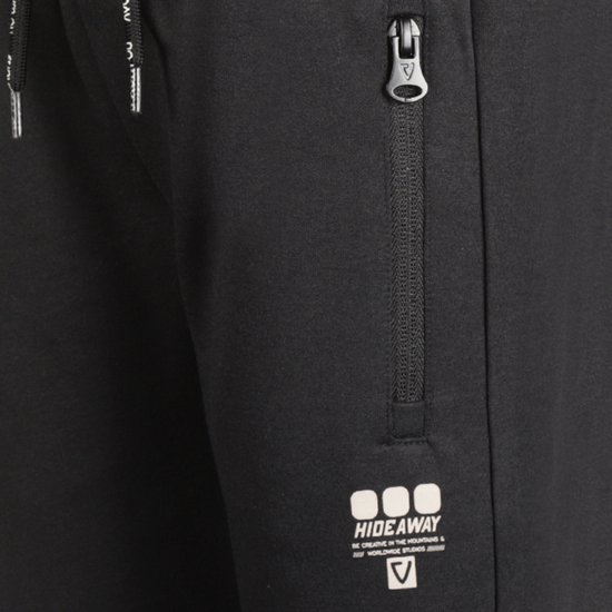 Detail van een zwarte joggingbroek met een zilveren ritssluiting en het 'HIDE away' logo.