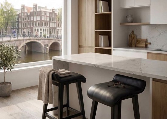 Twee zwarte barkrukken met een leren zitting en houten poten, voor een aanrecht met uitzicht op een gracht.