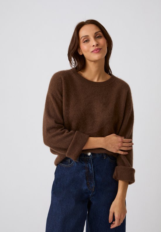 Model in een bruine geborstelde wollen trui en spijkerbroek.