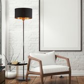 Zwarte staande lamp met koperkleurige binnenkant en een houten stoel ernaast.