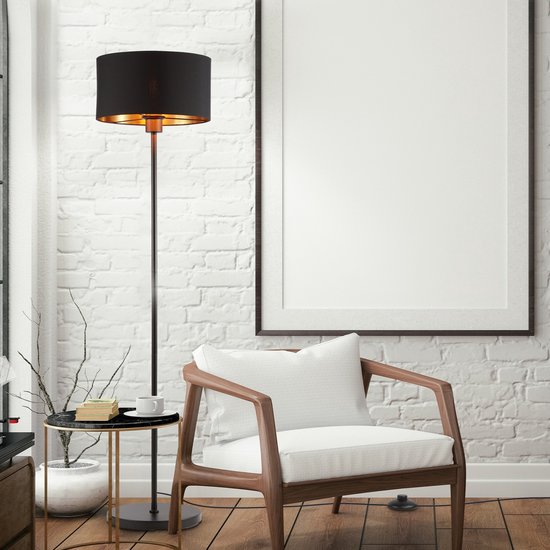 Lampe sur pied noire avec intérieur cuivré et une chaise en bois à côté.