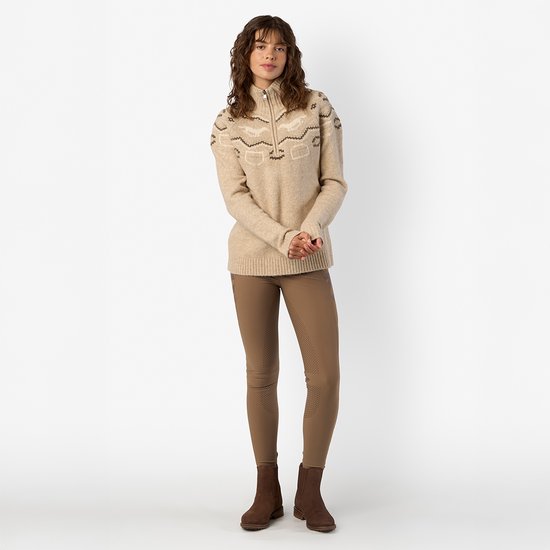 Model draagt een beige HV Polo trui met rits en geometrisch patroon, gecombineerd met bruine rijbroek en laarzen.