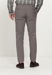 Zicht op de achterkant van een grijze chino broek gedragen door een man met een grijze geruite blouse en bruine sneakers.