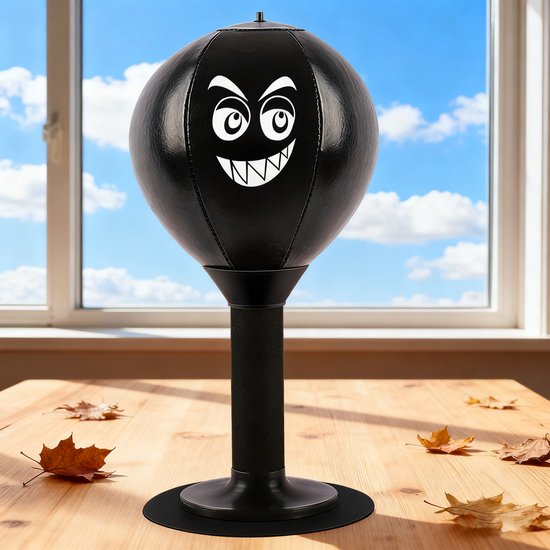 Zwarte desktop bokstrainer met boze gezicht, staand op een houten tafel met herfstbladeren.