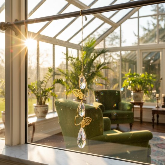 Gouden hanger met vlinders en druppelvormige kristallen, in een serre met zonlicht.
