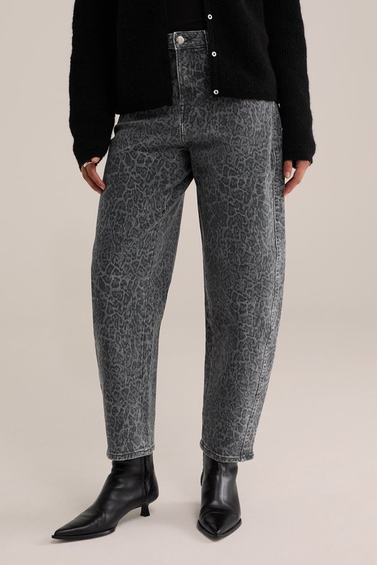 Model van voor met een grijze jeans met luipaardprint en zwarte laarzen.