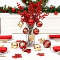 Een kersttafel gedekt met rode servetten en gouden bestek, met een vaas met rode bessen en kerstornamenten.