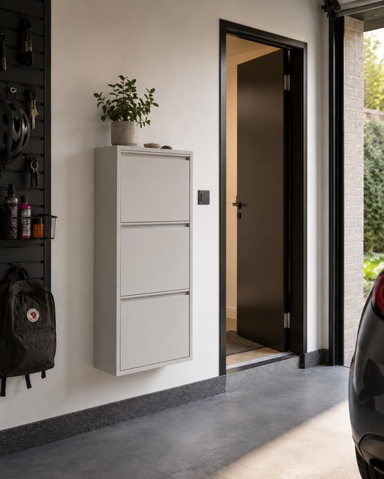 Witte schoenenkast met drie kleppen in een garage, naast een zwarte wand organizer met een helm en rugzak.