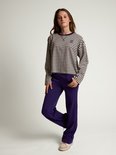 Model draagt een donkerpaarse broek en een gestreepte top met lange mouwen en een blauwe opdruk.