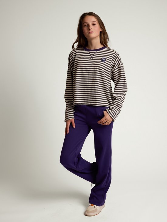 Model draagt een donkerpaarse broek en een gestreepte top met lange mouwen en een blauwe opdruk.