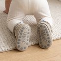 Baby op handen en knieën draagt taupe slofjes met antislip-zolen waarop de tekst Steppies staat.