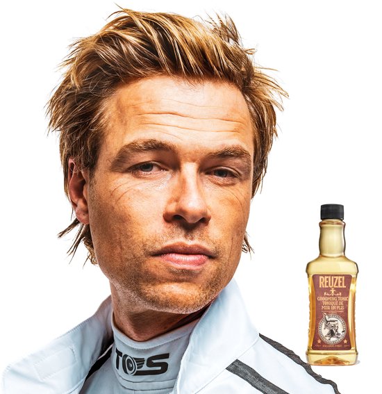 Man met warrig blond haar in racekleding naast een fles Reuzel Grooming Tonic.