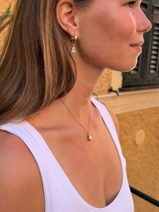 Model draagt een goudkleurige ketting met een kleine zirkonia-hanger en bijpassende druppelvormige oorringen.