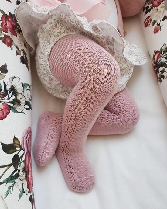 Baby in oudroze opengewerkte maillot, liggend op een bloemetjeslaken.