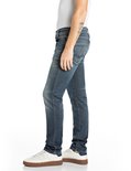 Zijaanzicht van een model in donkerblauwe Replay jeans, met tatoeage op de onderarm.