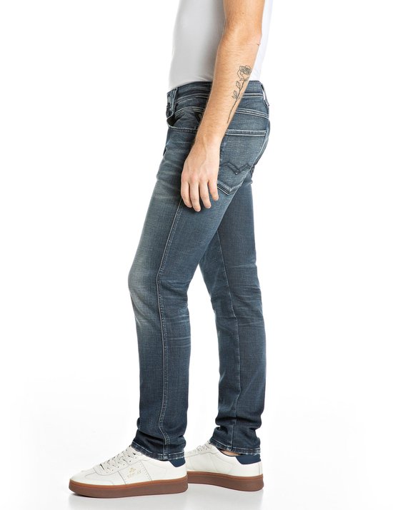 Zijaanzicht van een model in donkerblauwe Replay jeans, met tatoeage op de onderarm.