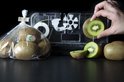 Een zak kiwi's en een hand die een kiwiplakje bij een transparant sealapparaat houdt.