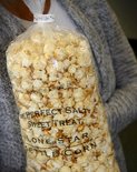 Een persoon houdt een zak popcorn vast, verzegeld met de Innoseal-sluiting, met tekst over de zoute en zoete smaak.
