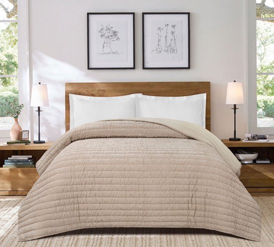 Zandkleurige Unique Living Didi sprei met horizontale stiksels op een houten bedframe in een slaapkamer.