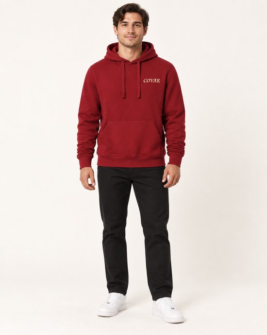 Man met zwarte broek, witte sneakers en rode COVAR hoodie met capuchon, staand.
