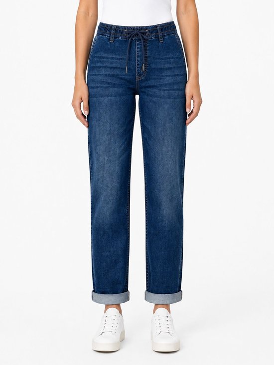 Donkerblauwe jeans met elastische tailleband, strikdetail en omgeslagen broekspijpen. Gedragen door een model met witte sneakers.