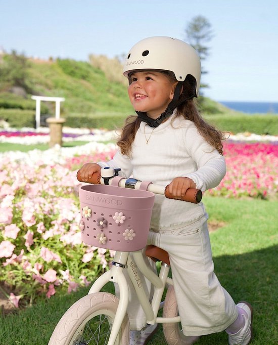 Lichtroze Banwood mandje met bloemen op het stuur van een kinderfiets.