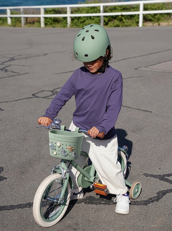 Kind op een groene Banwood fiets met een helm, voorop zit een groen mandje met accessoires.
